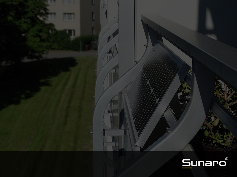 Balkonkraftwerk mit Solarmodul an einem modernen Metallgeländer, Blick auf gepflegte Rasenfläche