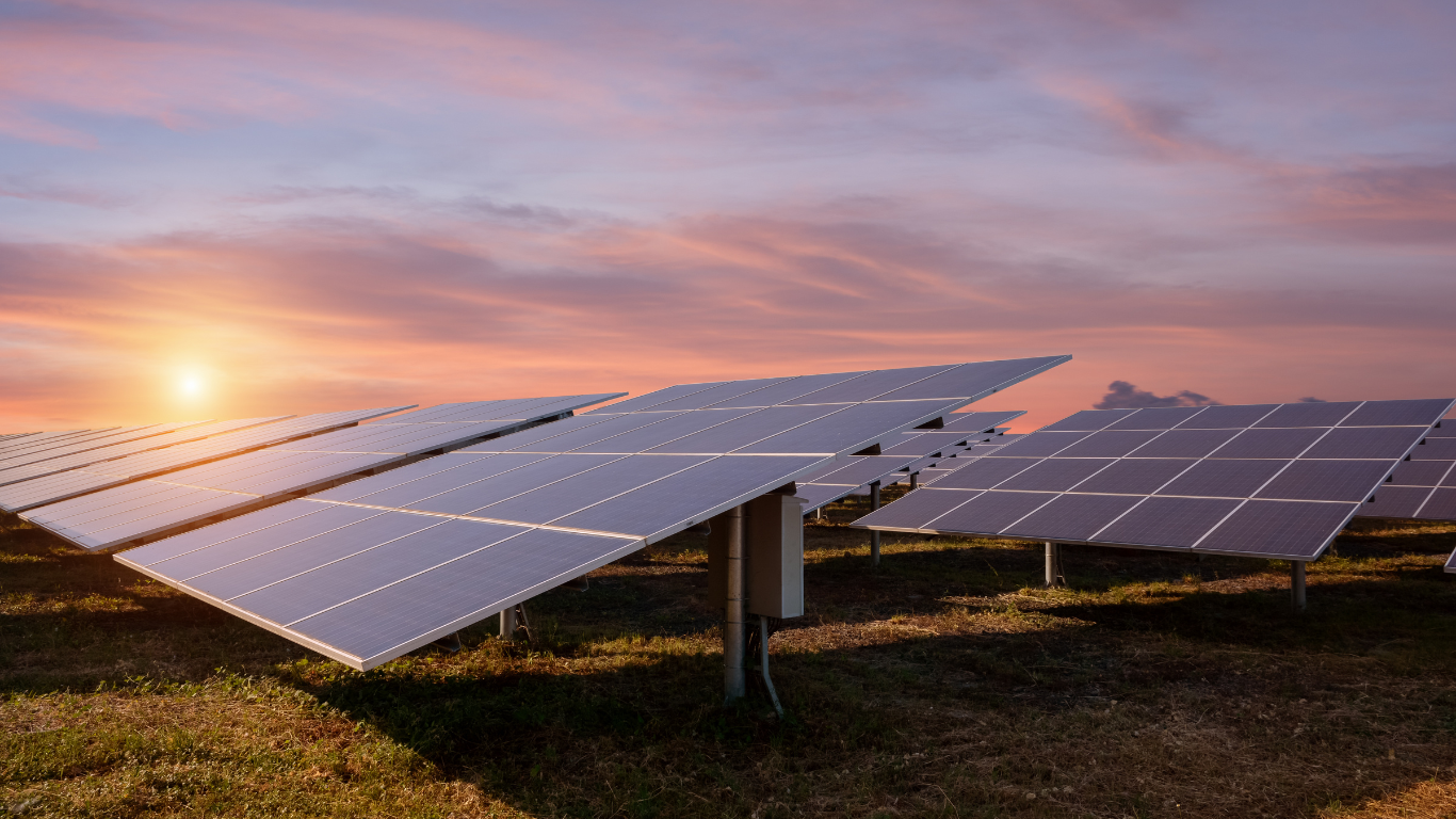 Solarmodule auf einem offenen Feld bei Sonnenuntergang mit violett-orangem Himmel