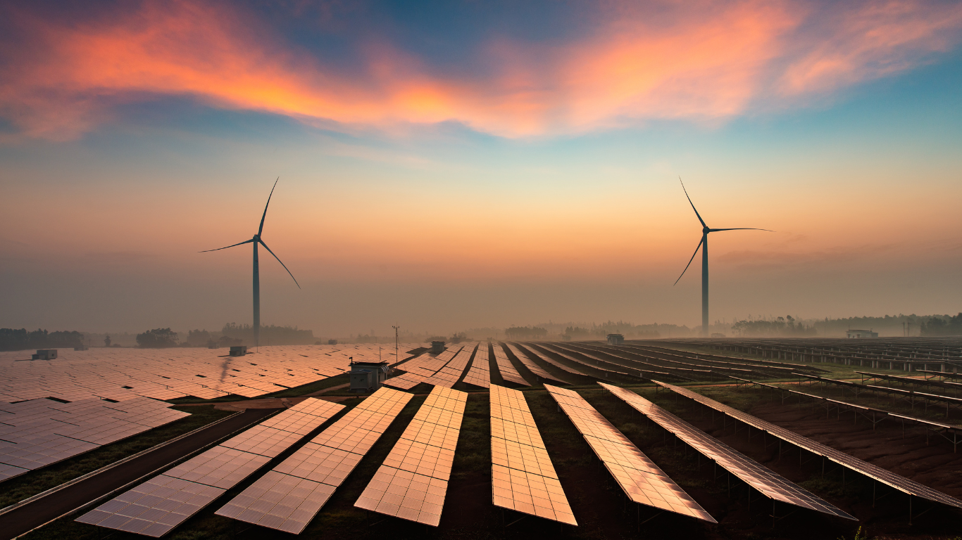 Solaranlage kombiniert mit Windkraftanlagen bei Sonnenaufgang und leicht nebeliger Atmosphäre.