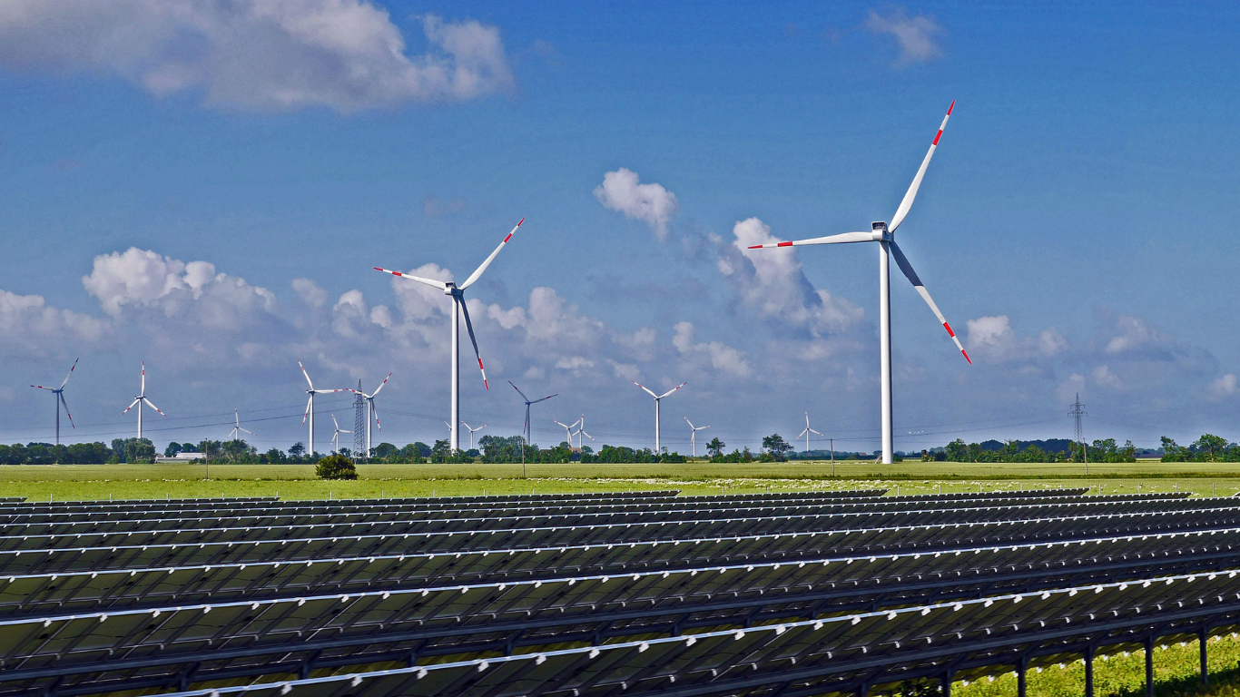 Windkraftanlagen und eine große Solaranlage mit bifazialen Solarmodulen auf einer grünen Wiese unter blauem Himmel