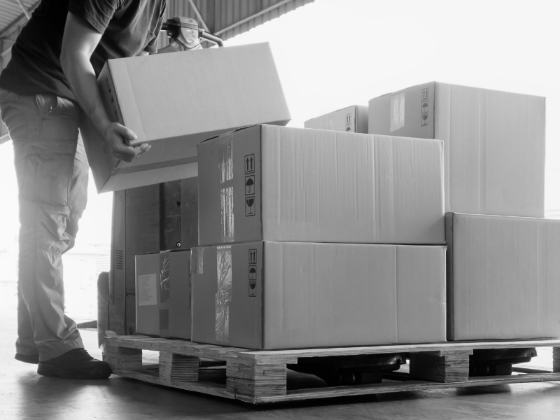 Mitarbeiter hebt Pakete in der Lagerhalle – Exoskelett zur Rückenentlastung in der Logistik